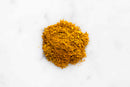A small mound of golden-yellow World Spice Continental Curry is scattered on a white marble surface.
