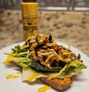 An open-faced sandwich with mixed greens, cheese, and saucy grilled mushrooms on rustic bread, drizzled with Terrapin Ridge Farms Coconut Curry Aioli. A bottle of Terrapin Ridge Farms Coconut Curry Aioli is in the blurred background.