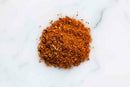 A small pile of World Spice Pakistani Curry, a reddish-brown blend rich with aromatic spices, is scattered on a white marble surface.