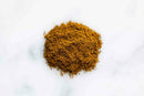 A small pile of World Spice Turkish Curry, a ground brown spice blend from World Spice, sits on a white marble surface.