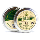 Two round metal tins of The Spice Lab Hemp Leaf Sprinkles CBD & THC Free sit side by side, making them ideal for edible party decorations. The labels prominently declare “CBD & THC Free,” highlighting that the sprinkles are edible and drug-free. Adorned with green hemp leaves and decorative details, one tin showcases the front label while the other displays the back.