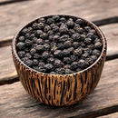 A small wooden bowl filled with The Spice Lab Organic Black Tellicherry Peppercorns Whole sits on a rustic wooden surface.