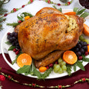 A roasted turkey stuffed with dressing seasoned with The Spice Lab Organic Rubbed Sage sits on a platter, garnished with grapes, cranberries, orange slices, and herbs. A festive tablecloth and holiday decorations are visible around the platter.