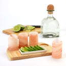 A bottle of liquor, sliced limes on a cutting board, and four The Spice Lab Tequila Himalayan Salt Shooters by The Spice Lab are arranged on a small wooden tray with lime wedges in a dish.