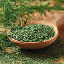 A wooden spoon filled with The Spice Lab Dill Weed Whole, resting on a table with fresh dill sprigs in the background—perfect for delivering authentic flavor to any bulk foodservice herb selection from The Spice Lab.