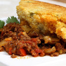 A serving of savory ground beef and vegetables, seasoned with The Spice Lab Organic Chili Powder Blend by The Spice Lab, topped with a golden, crumbly cornbread crust and garnished with fresh cilantro, on a white plate.