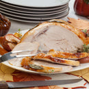 Sliced roast turkey breast on a platter, garnished with The Spice Lab Organic Rubbed Sage and fresh herbs, with serving utensils. Stacked plates and autumn-themed decor are visible in the background.