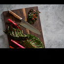 The Steelport Knife Co. 8" Chef Knife, acclaimed for its exceptional blade edge retention owing to traditional forging methods, rests beside vibrant bundles of Swiss chard on a dark wooden cutting board atop a gray countertop.