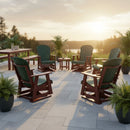 A sunlit patio displays six Kanyon Living Adirondack Poly Glider Swivel Chairs in dark green & cherry, arranged in a circle among potted plants and tables, offering scenic views of trees and water at sunset.