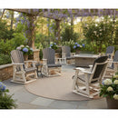 A cozy patio features Kanyon Living Adirondack Poly Glider Swivel Chairs in Driftwood Grey & White around a fire pit table, with lush greenery, blooming hydrangeas, and wisteria hanging from the pergola for supreme outdoor comfort.