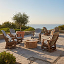 Six Kanyon Living Adirondack Poly Glider Swivel Chairs in Light Grey & Weathered Wood are arranged around a round coffee table on a stone patio, offering sustainable outdoor comfort with lush greenery, ocean views, and a large potted tree.