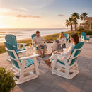 Three people relax and chat at sunset on Kanyon Living Adirondack Poly Glider Swivel Chairs in Aruba Blue & White by the beach, with palm trees and a calm ocean providing a scenic backdrop.