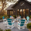 A family of five relaxes in Kanyon Living Adirondack Poly Glider Swivel Chairs in Aruba Blue & White, chatting around a patio table at sunset outside a dark wood house, with potted plants and drinks adding to the inviting outdoor scene.