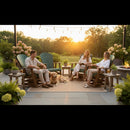 Three people relax on Kanyon Living Adirondack Poly Glider Swivel Chairs in Dark Green & Cedar around a rug with a golden retriever at their feet on a patio with plants, under string lights and a sunset beyond the trees.