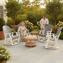 A woman and a man relax on a patio surrounded by greenery, enjoying outdoor comfort in Kanyon Living Adirondack Poly Glider Swivel Chairs in Driftwood Grey & White—stylish, recycled HDPE furniture by Kanyon Living.