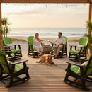 A man and woman relax on Kanyon Living Adirondack Poly Glider Swivel Chairs in Lime Green & Black by a fire pit on a beachside deck, surrounded by outdoor furniture, potted plants, string lights, their golden retriever, and an ocean view.