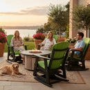 Three people relax in Kanyon Living Adirondack Poly Glider Swivel Chairs (Lime Green & Black) on the patio by a fire pit, chatting. A golden retriever rests nearby, with potted plants and a lake reflecting the sunset in the background.