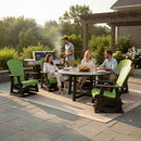 Four people relax outdoors on a patio with Kanyon Living Adirondack Poly Glider Swivel Chairs in lime green & black around a round table. One grills nearby, all enjoying sunshine and greenery—the ideal setting for Kanyon Living quality.