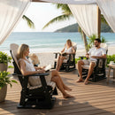 Three people relax on Kanyon Living Adirondack Poly Glider Swivel Chairs in Seashell & Black under a canopy on a beachside deck, reading and smiling with palm trees, white curtains, and the ocean in the background.