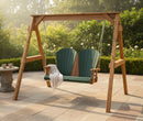 The Kanyon Living Poly Lumber 4′ Adirondack Swing in Dark Green and Cedar Wood sits on a tiled patio, draped with a white blanket. Two cups rest on a stone table nearby, surrounded by lush garden greenery.