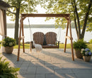 The Kanyon Living Poly Lumber 4′ Adirondack Swing Deluxe in Antique Mahogany and Black offers inviting outdoor seating for two on the patio, accented with a white blanket and potted plants—perfect for relaxing by the lakeside.