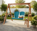 The Kanyon Living Poly Lumber 4′ Adirondack Swing in Aruba Blue & White features two seats and sits on a patio rug with a pillow, book, and mug. A wooden side table stands nearby among green plants and a white fence.