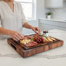 A woman arranges meats, cheeses, grapes, crackers, and jam on the Best BBQ Board® 16 x 12 Cutting Board by BBQ Boards® in a bright, modern kitchen.