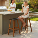 Two women enjoy a sunny outdoor kitchen. One relaxes on a Kanyon Living Poly Lumber Saddle Stool Bar Height in Black and Deluxe Antique Mahogany at the counter, while the other stands behind it, smiling near fruit and a pitcher.