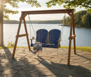 The Kanyon Living Poly Lumber 4′ Adirondack Swing in Blue and Light Grey sits on a stone patio by the lake, shaded by trees. A striped blanket, open book, and coffee mug evoke peace with this eco-friendly Kanyon Living furniture.