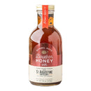 A glass bottle of Honey Truck Co Raw Bourbon Infused Wildflower Honey, crafted with rich wildflower honey and bourbon from St. Augustine Distillery. This amber liquid comes in an 18 oz (510g) bottle featuring a tan label and an orange “Honey Truck Co.” tag around the neck.