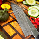 A Spaceman Knives Calypso Chef Knife by Spaceman Knives rests on a wooden cutting board, surrounded by sliced cucumbers, red chili peppers, yellow tomatoes, and small green squash—showcasing expert food prep in action.