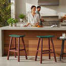 A woman smiles at an outdoor counter with food, while a man cooks nearby. Two Kanyon Living Poly Lumber Saddle Stool Bar Height stools in Dark Green and Cherry Wood add comfort and style to the scene.