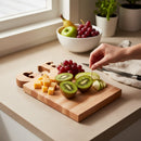 A hand uses a toothpick to pick up a green apple slice from the Words With Boards Gluten Free Personalized Cutting Board (6 1/4" x 9 1/2") by Words with Boards, LLC, surrounded by kiwi halves, cheese cubes, grapes, and more apple slices.