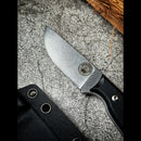 The Spaceman Knives Halimede Fixed Blade Knife features a D2 steel blade and black Micarta handle with stamped logo, shown on a gray surface beside its black riveted sheath and pieces of straw.
