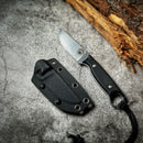 The Spaceman Knives Halimede Fixed Blade Knife, featuring a durable Micarta handle and finger ring, rests beside its black sheath on a textured gray surface, with rough wood visible in the upper right corner.