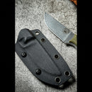 The Spaceman Knives Halimede Fixed Blade Knife, featuring a rugged Micarta handle and stonewashed D2 steel blade, rests beside its black molded sheath on a rough gray surface.
