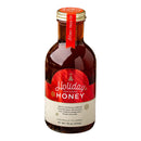 A glass bottle of Honey Truck Co Holiday Honey® by Honey Truck Co, adorned with a red and cream label featuring festive details. The label highlights flavors of cinnamon, cloves, and citrus, and notes that the honey is minimally filtered—making it an ideal Christmas gift or special Holiday Honey treat.