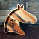 The Wooden Horse Head Serving Tray With Custom Engraving Options by Two Acre Woodworks features multicolored wood strips and can be personalized with a name and number in a laurel wreath, making it unique against any rustic wooden backdrop.