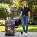 A woman in a black t-shirt and jeans stands outdoors by a round charcoal grill, next to a Jealous Devil Max XL Briquettes 20 lb bag (Pallet of 48 bags) with bold red and white graphics.