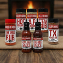 The Killer Hogs BBQ Rub and Sauce Complete Gift Set features an array of Killer Hogs seasonings and sauces with distinctive red, white, and black labels, all arranged on burlap in front of a fireplace.