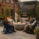 Five people relax on Kanyon Living Adirondack Poly Glider Swivel Chairs in orange & black around a fire pit on a stone terrace. One woman grills while others chat, surrounded by string lights, greenery, and a log cabin backdrop.
