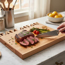 A hand slices cooked steak on the Words With Boards Seriously Gluten Free Personalized Cutting Board (Small, 9.5" x 12.5") by Words with Boards, LLC. Asparagus, cherry tomatoes, and grilled garlic are nearby; utensils and lemons are in the background.
