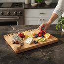 A hand reaches for a strawberry on the Words With Boards Seriously Kosher Personalized Cutting Board (Large 16” x 12.5") by Words with Boards, LLC, engraved with MEGAN & JON and KOSHER, surrounded by cheeses, fruits, and crackers.