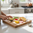 In a bright kitchen, someone slices an avocado on the Words With Boards Wedding Bells Personalized Cutting Board by Words with Boards, LLC, surrounded by toast, radishes, tomatoes, lemon wedges, rosemary, and a bowl of salt.