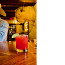 DDR BBQ Supply prickly pear cocktail with a lime wedge garnish on a wooden bar in a rustic western-style setting