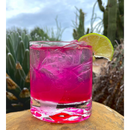DDR BBQ Supply prickly pear cocktail with a lime garnish in a glass against a desert cactus background