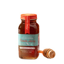 A jar of Honey Truck Co Raw Florida Wildflower Honey, featuring a teal and red label, sits next to a wooden honey dipper against a white background.