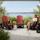 A woman smiles as she sits on a Kanyon Living Adirondack Poly Glider Swivel Chair in Red & Black by Kanyon Living, enjoying a sunny patio with lake views, additional outdoor seating, and lush greenery around her.
