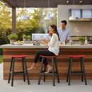 A woman sits on a Kanyon Living Poly Lumber Saddle Stool Bar Height Red and Black at an outdoor kitchen island, smiling at a man behind the counter as they enjoy drinks, food, and a modern patio setting with plants and grilling supplies.