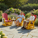 A man and woman sit on Kanyon Living Adirondack Poly Glider Swivel Chairs in red and yellow, enjoying lemonade at a small table in a garden with flowering bushes, smiling and talking.